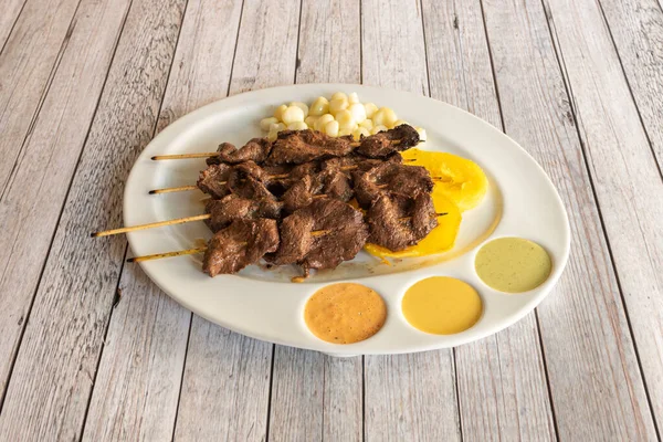 Izgarada pişirilmiş mısır, patates ve soslu tatlı patatesle pişirilmiş ahşap çubuklara batırılmış bir tepsi Peru hamsi.