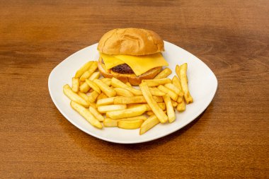 Çedar peynirli, hardallı ve ketçaplı leziz klasik sığır burger ve beyaz tabakta patates kızartması.