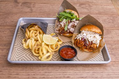 Taze peynir, roka, barbekü sosu ve sarmal patates kızartmasıyla dilimlenmiş iki biftek ve domuz burger tabağı.