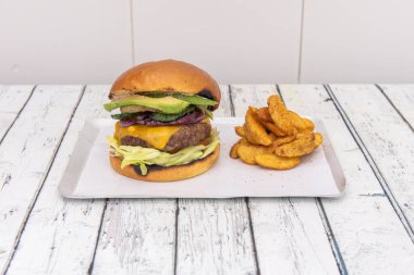 Bir sürü avokado, kırmızı soğan, marul, çedar peyniri, biber ve yanında patates kızartması olan Küba usulü etli burger.