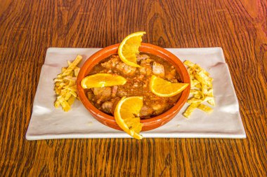 Turuncu domuz etli güveç ve beyaz tabakta patates kızartması.