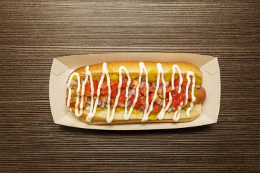 Hot dog in cardboard container with toppings with mayonnaise and mustard