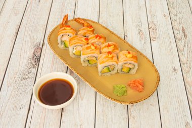 Uramaki dragon roll on  salmon, cooked prawns and raw avocado with soy sauce, wasabi and ginseng on wooden table