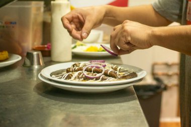 Şefin elleri, metal mutfak yüzeyinde mor soğan halkaları olan bir tabak hazırlıyor.