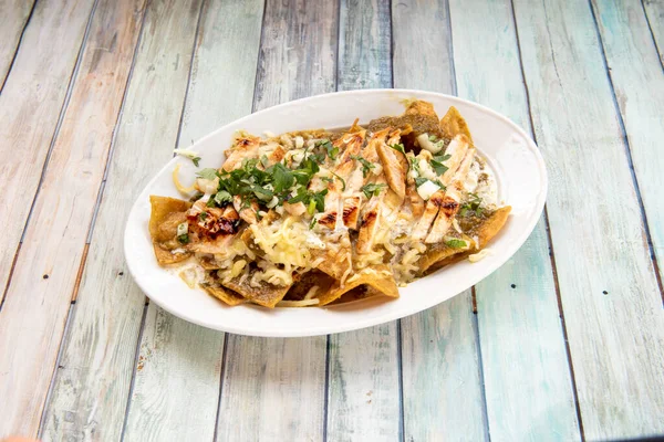 spicy Mexican chilaquiles recipe, with stewed chicken, corn chips and melted cheese with coriander on top