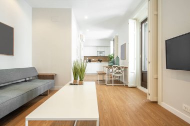 Televizyon, kanepe ve geniş pencereli oturma odası, arka planda, ofis ve mutfak kiralık bir stüdyoda.