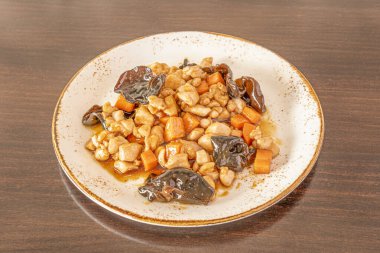 Çin mantarlı tavuk yemeği, sebze ve yakisoba sosu beyaz tabakta kahverengi kenarlı.