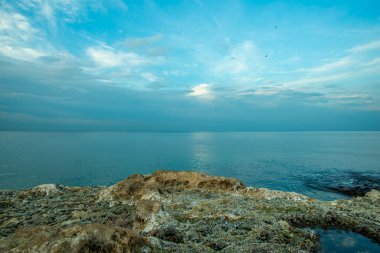 Türk Karadeniz kıyısında gün batımında kayalar var. Sahilde bulutlu sakin bir gün.