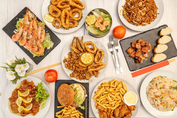 Top view image of Chinese-Spanish fusion dishes with wok stir-fry noodles, tres delicias rice, Andalusian fish fry, grilled shrimp, battered squid rings, lemon chicken, and torrezno