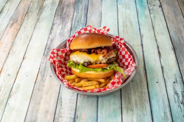 Bol peynirli çizburger sever, kızarmış domuz pastırması, marul, domates ve patates kızartması yatağında biftek.