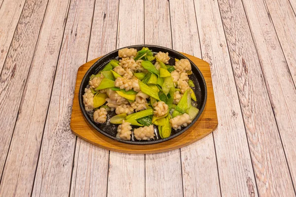 Chinese recipe of wok fried squid dish with vegetables on bamboo tray on white table