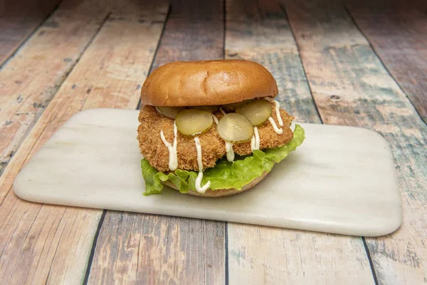 Crispy chicken burger with pickles and mayonnaise sauce with lettuce on white marble plate