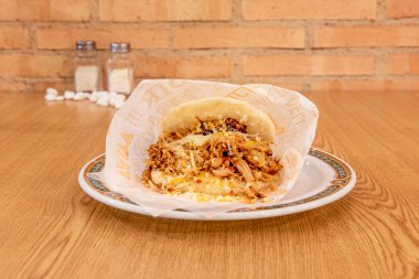 Venezuelan arepa of shredded chicken meat with fresh grated cheese on wooden table
