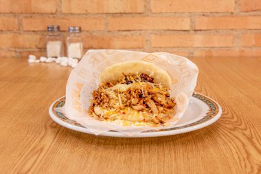 Venezuelan arepa of shredded chicken meat with fresh grated cheese on wooden table clipart