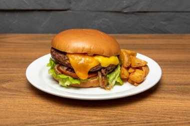 Eritilmiş çedar peynirli sığır burger, hardal, kızarmış soğan, domates, marul ve kızarmış patates dilimleri.