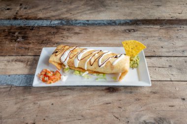 Beef chimichanga with avocado and tortilla chips with pico de gallo on wooden table