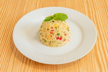 Couscous taboule with vegetables and good herb on the white plate.