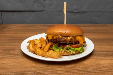 Erimiş çedar peyniri, karamelli soğan, domates ve hardallı mangalda sığır burger ve patates kızartması.