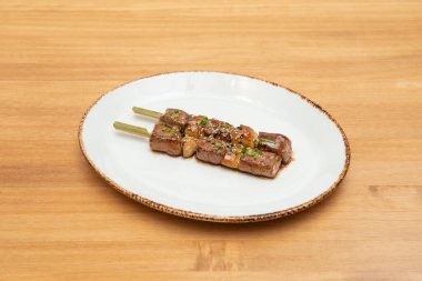 Sebzeli tavuk şişi, yakitori, beyaz bir tabakta yakisoba sosu susam tohumları, haşhaş ve doğranmış soğan.