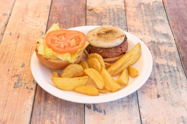 Etli vejetaryen burger yanında ızgara beyaz soğan halkaları, domates, marul ve kızarmış patates dilimleri.