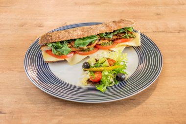 Ciabatta ekmekli sandviç kızarmış tavuk, lahana, fesleğen, kapuçin sosu, domates ve peynirli siyah zeytin, turşulu piparra ve marul.