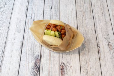 Bao ekmekli sandviç, tatlı ve ekşi sosla marine edilmiş tavuk, soğan soğanı ve kahverengi parşömen kağıdına sarılmış çiğ salatalık.