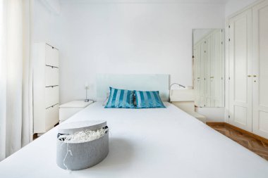 Büyük boy yataklı, mavi yastıklı ve kiralık bir dairede beyaz mobilyalı bir oda.