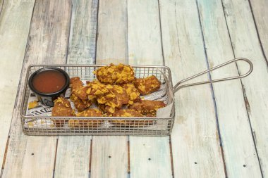 Panko ve ahşap masa üzerinde barbekü soslu ekmek arası metal sepet.