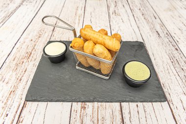 Peynir örgü ve domuz pastırması dolu metal sepet kişniş süslemeli muz yapraklarından bir yatakta sunuluyor.