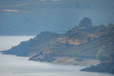 Gökyüzünün altındaki kayalık tepelerle çevrili zümrüt sularıyla panoramik bir yer.