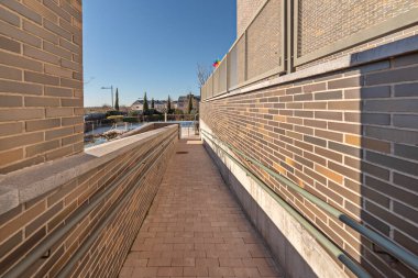 Katı tuğladan duvarları, açıkta duran ahşap kirişleri ve zemin drenaj sistemi olan binalar arasında bağlantı koridoru.