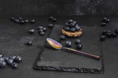 Taze toplanmış yaban mersini ile siyah ipek arka planda sabah çiği ve altın detaylarıyla porselen bir kaşık.