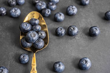 Siyah deri arka planda, meyvelerin mor tonlarını vurgulayan nikel gümüş kaşıkla mükemmel yaban mersinlerinin yakın çekimi.