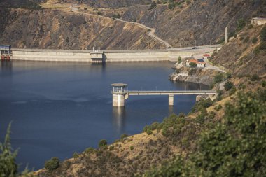  Sonbaharda yaprak döken ağaçlarla dolu bir baraj. Sakin, karanlık sulara yansıyan altın ve kırmızımsı renklerini sergiliyorlar.