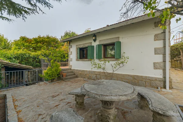 Terasta doğal fiber yemek masası düzensiz bir taş cephesi ve saksılarda Japon kemerlerinin gölgesi var.