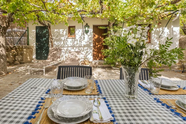 Terrazzo masalı yemek takımı ve salkımlı ahşap pergola altında geri dönüştürülmüş plastik sandalyeler.