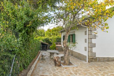 Oval bir masa ile demir yemek seti ve taş duvarlı minderli sandalyeler ve yasemin tırmanışı.