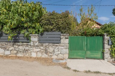 Metal kapılı taştan bir duvar, yeşile boyanmış, tipik bir kır evi..