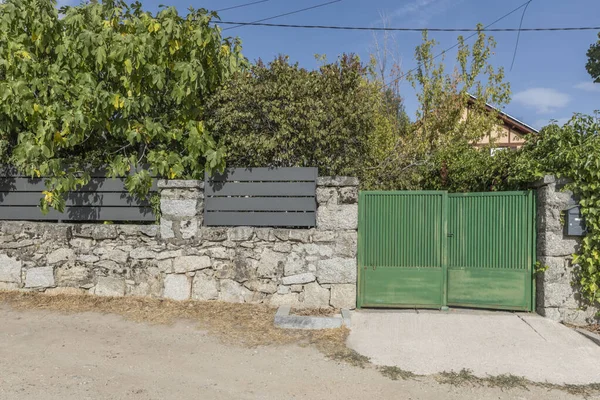 Metal kapılı taştan bir duvar, yeşile boyanmış, tipik bir kır evi..