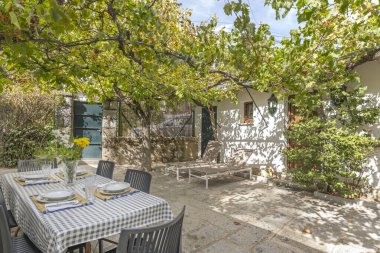 Bazalt masalı yemek takımı ve geniş bir Sibirya karaağacının gölgesinin altında sıralar.