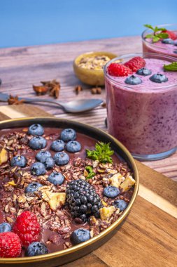 Sabah ışığının doğal yansımaları taze yaban mersinlerinin çiğ tanelerini yakalar ve meyve suyu ile tahtanın tahtalarındaki tahıl gevreği arasındaki dokularını güçlendirir.