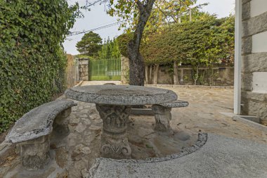 Bir mozaik masası olan açık hava yemek seti ve taş duvarlı bir terasta reçine sandalyeleri ve limon ağaçları.