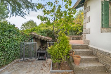 Yıllanmış granit duvarlı dış geçit ve eskimiş tırmanma gülleri taşın sağlamlığıyla çiçeklerin zarafetini birleştirir..