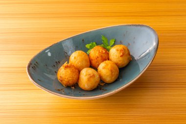 Yeşil aonori yosunuyla süslenmiş sekiz parça takoyaki ve bambu tabakta tatlı sos.