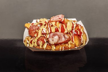 Klasik ızgara domuz sosisi ve ev yapımı patates kızartması kombinasyonu ahşap tabakta hardal ve ev yapımı mayonezle servis ediliyor.