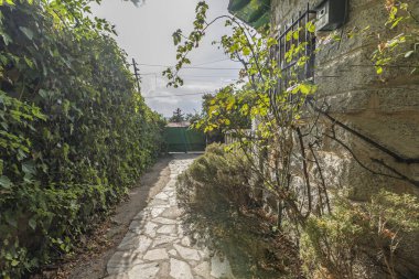 Granit alçak duvarlı bir bahçe geçidi. Oturma yeri ve adaçayı çiçeği yatağı görevi görüyor. Evin içi ve dışı arasında geçiş alanı yaratıyor.