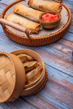 Yumurta rulolarının yüksek açılı fotoğrafları balık sosu ve limon kaselerinin yanında dokulu keten masa örtüsünün üzerinde bir buhar sepetinde servis ediliyor.