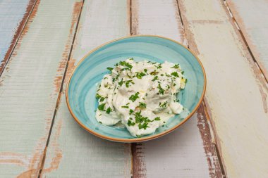 Cömert bir kase düzensiz şekilli haşlanmış patates sunulur, kremalı ev yapımı aioli sosuyla kaplanır, taze doğranmış maydanoz ve bir tutam tatlı kırmızı biber ile süslenir..