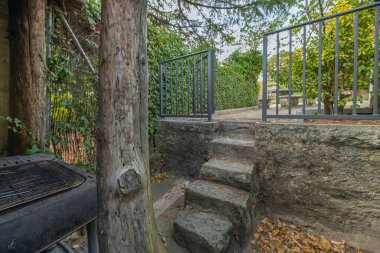 Granit döşemeli bir yan koridor ve kısmen sarmaşık tırmanışı ile kaplı doğal bir taş duvar bitki örtüsünü mimariye entegre eder.