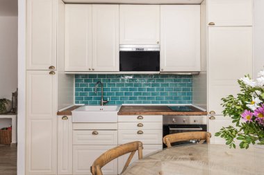 Doğal ketenle döşenmiş sandalyeli yuvarlak, sert meşe masa ve el yapımı seramik vazoda gümüş okaliptüslü bir buket gardenya gülü gül.